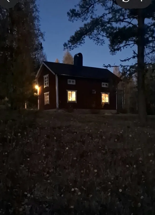 En stuga med upplysta fönster i skymningen.